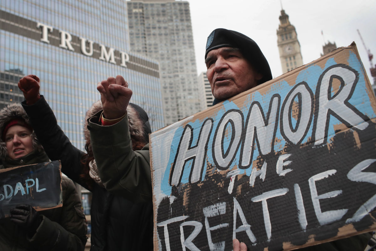 A man holds a sign reading "HONOR THE TREATIES" during a protest