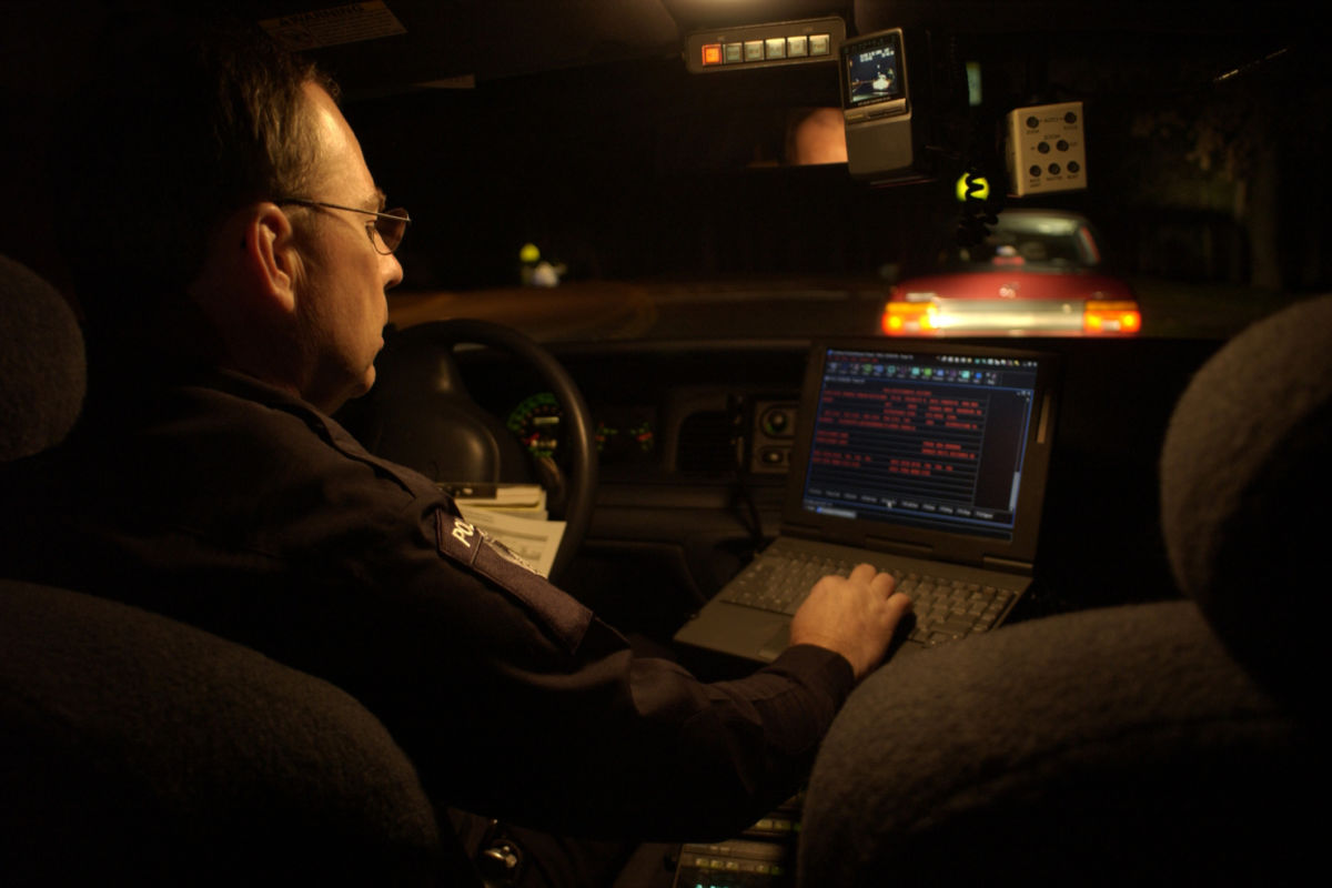 A police officer views a laptop screen while in his cruiser