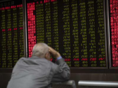 A man holds his head while watching stock prices on a lit screen