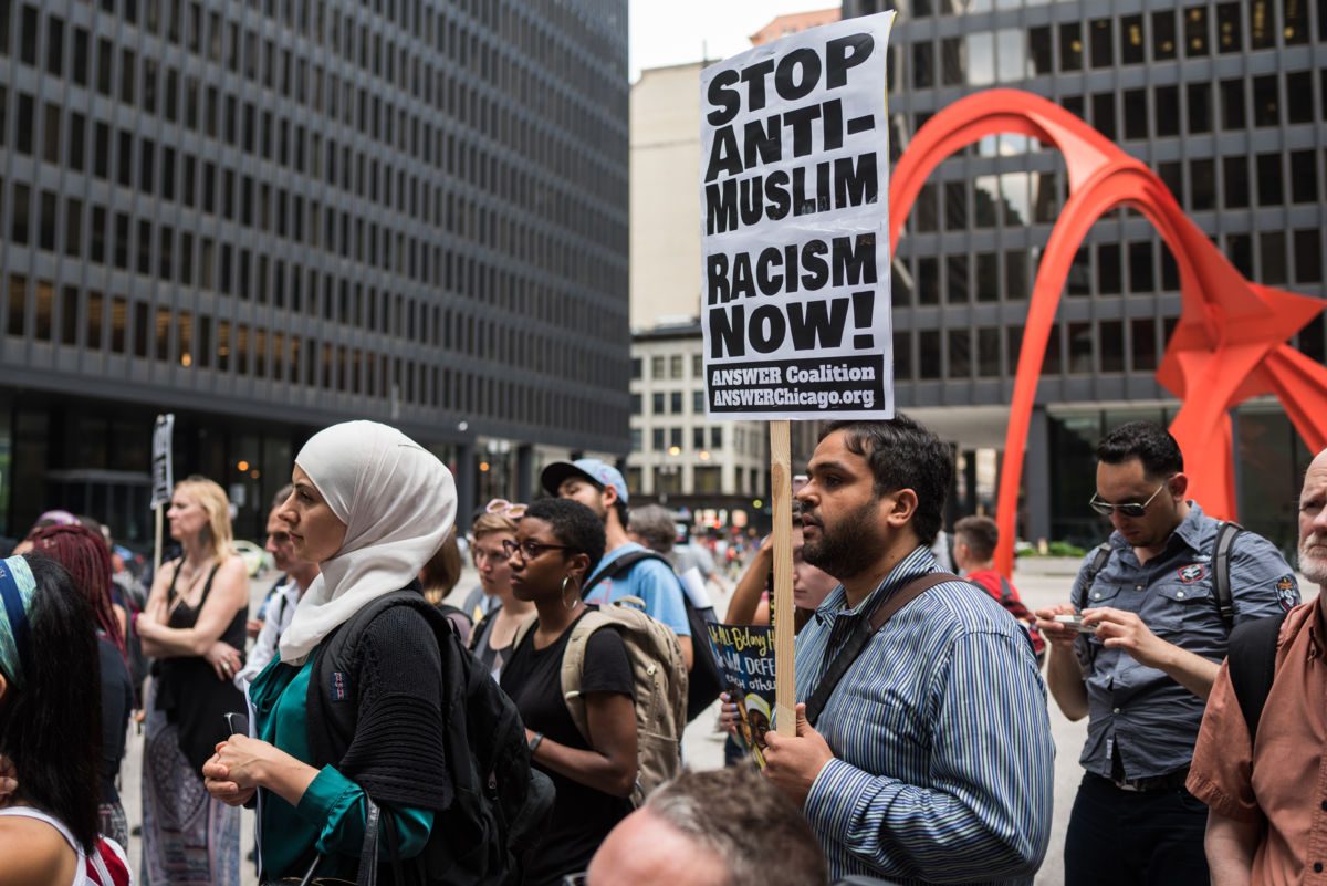 Muslim protesters display signs in front of a large orange statue