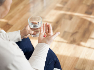 A person holds pills in one hand and a glass of water in the other
