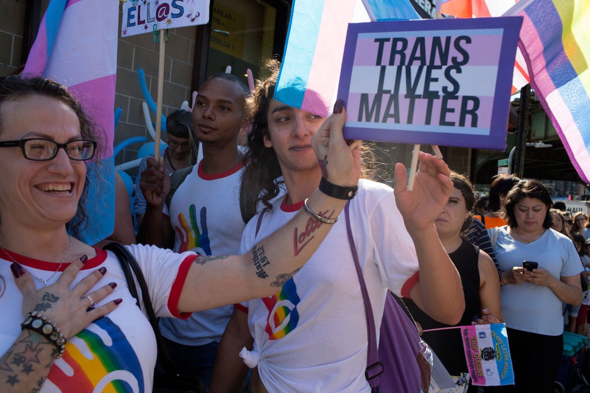 People hold "TRANS LIVES MATTER" signs while protesting, transgender