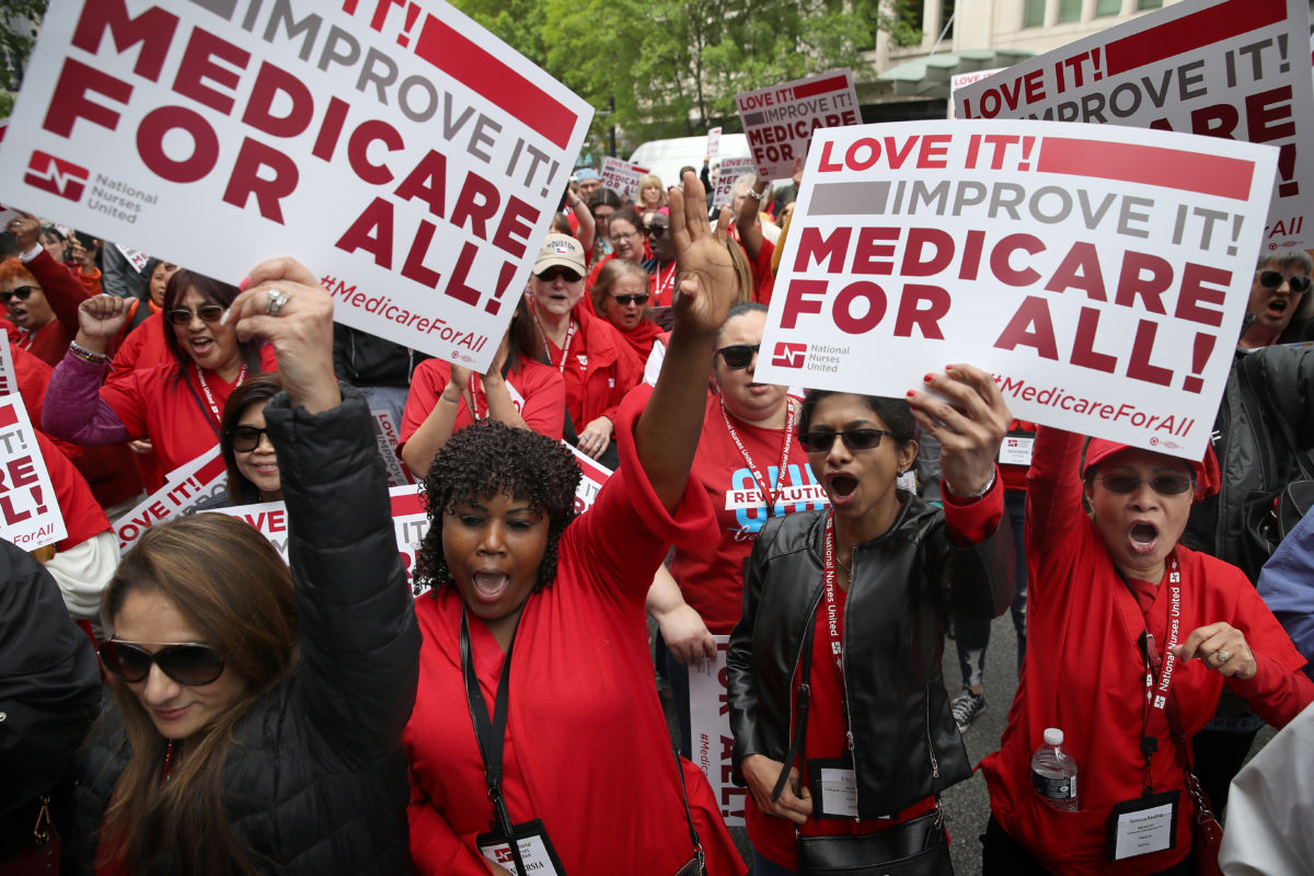 People dressed in red protest while holding "Medicare for all" signs