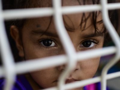 A child looks through wire mesh, immigration, migrants