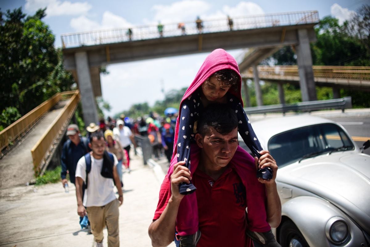 A father carries his daugher on his shoulders as he walks with other migrants down a highway