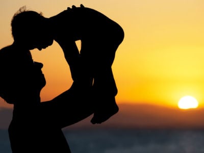 Father lifts child, silhouetted against sunset
