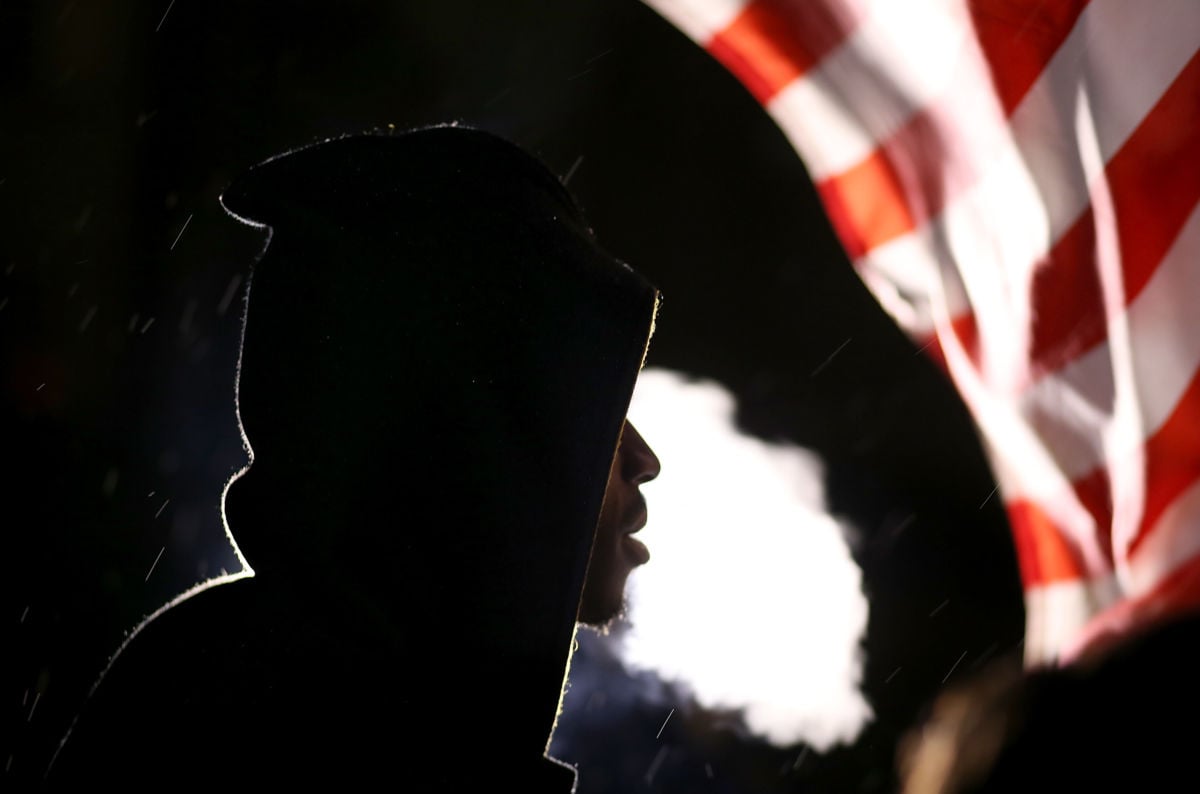 Fog rises from a young man as he breathes with a U.S. flag in the background
