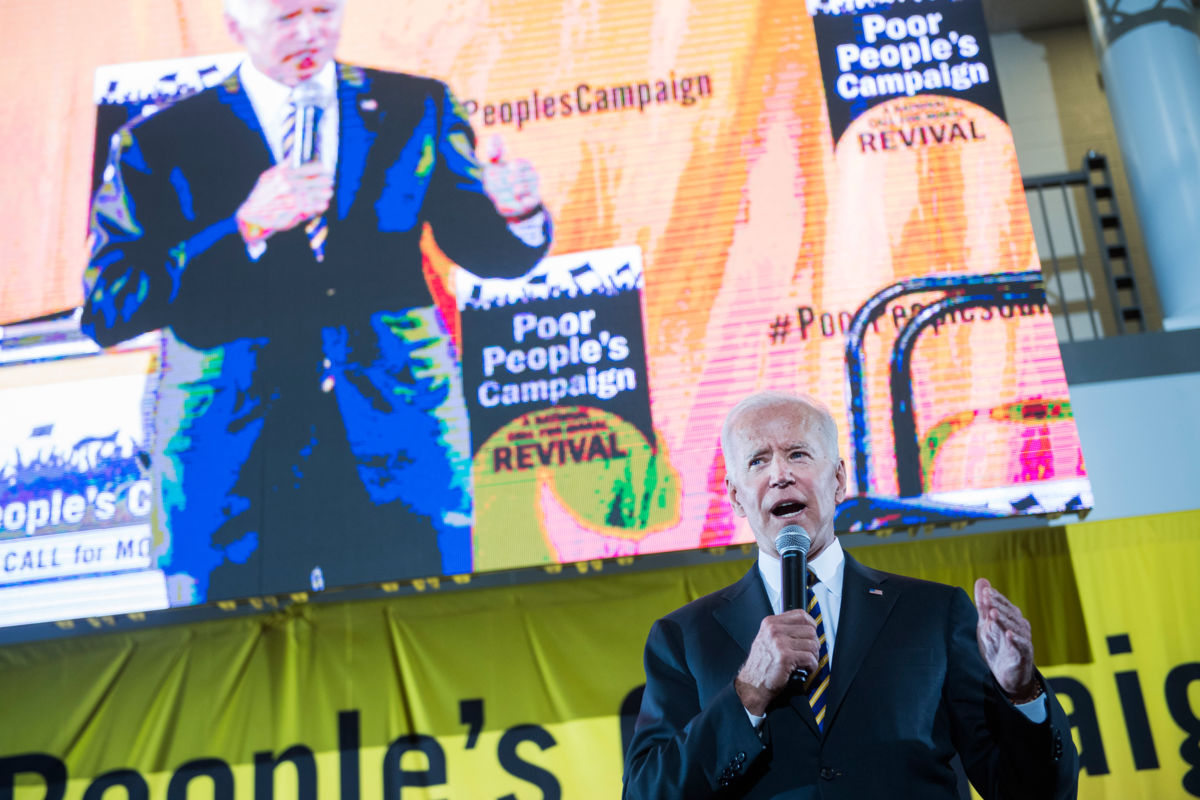 Joe Biden speaks in front of a loudly colored display screen also displaying his likeness