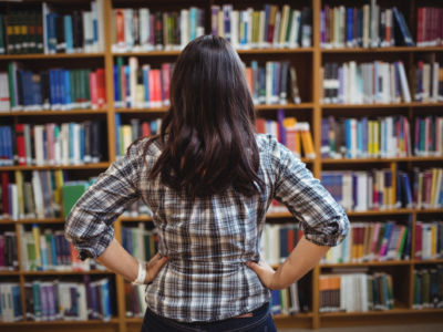 A young woman looks at shelves of books in a library