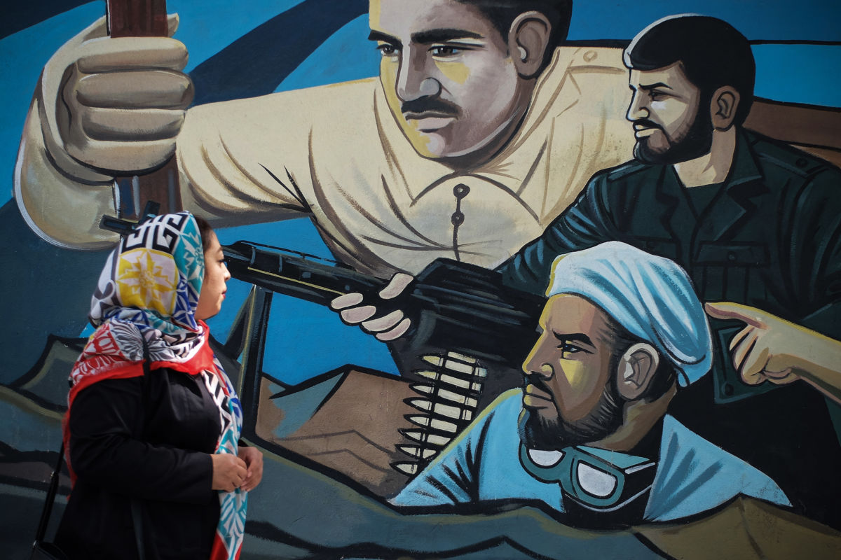 A woman in a hijab looks at a mural depicting several soldiers fighting