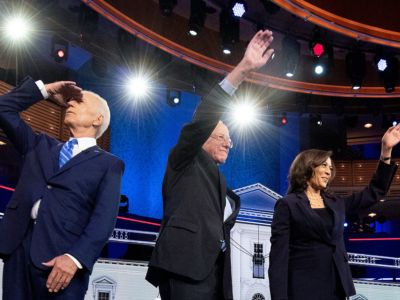 Joe Biden stares into lights as Bernie Sanders and Kamala Harris wave to the audience in front of them