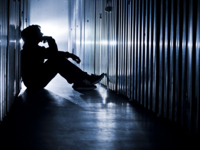 A youth sits amidst cells while silhouetted by blue light