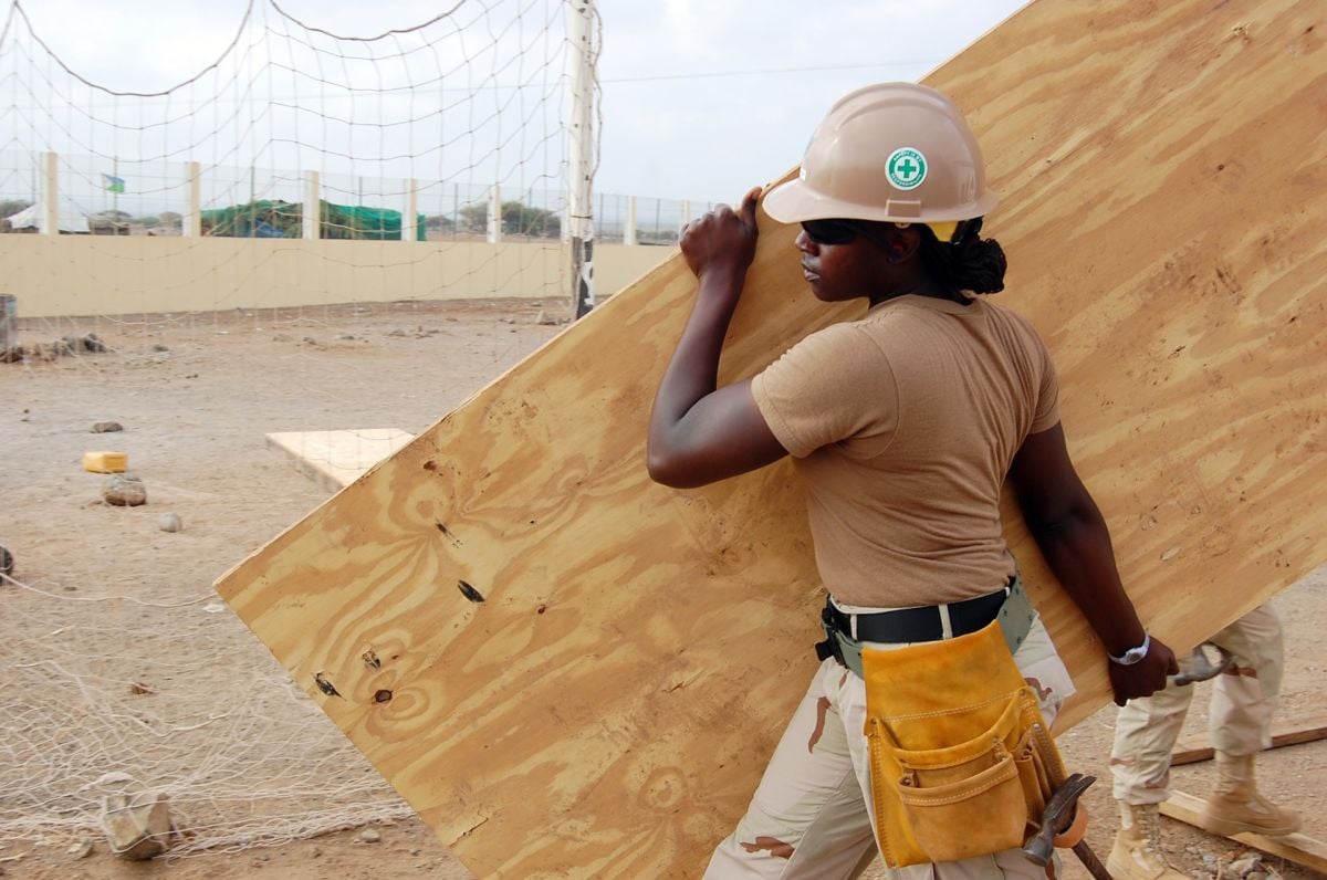 A Black construction worker carrying plywood.