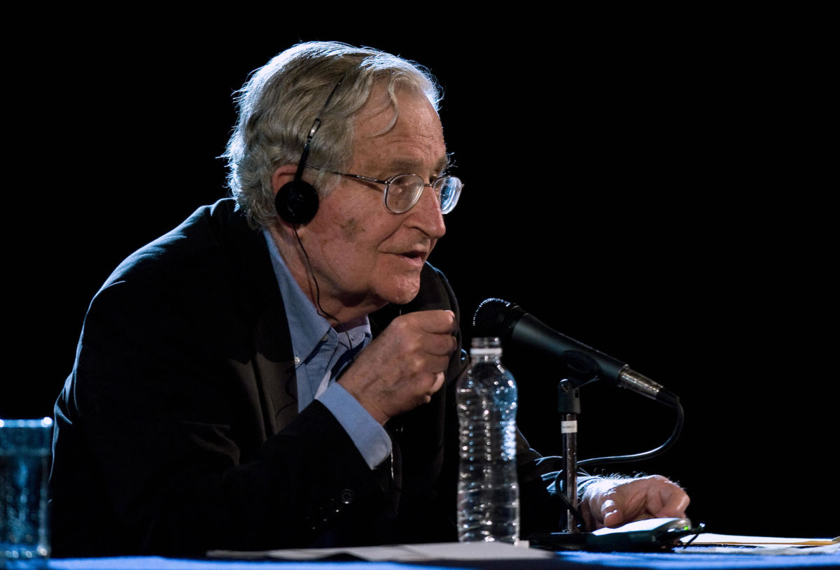 Noam Chomsky speaks into a microphone while seated