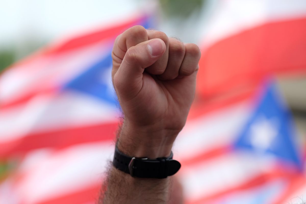 A demonstrator raises a fist during a protest with Puerto Rican flags billowing behind hin