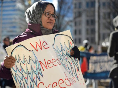 A hijabi holds a sign reading "We deserve freedom" during a protest