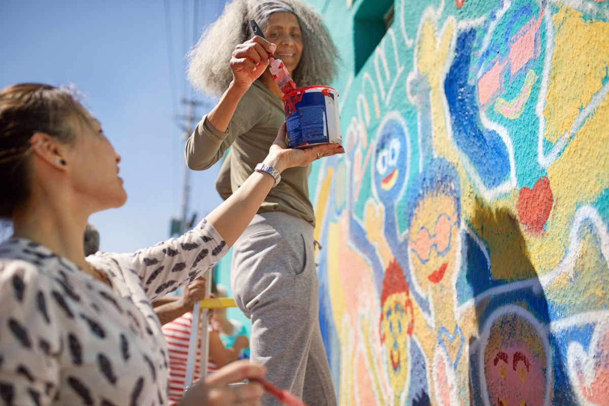 Volunteers painting vibrant community mural on sunny urban wall