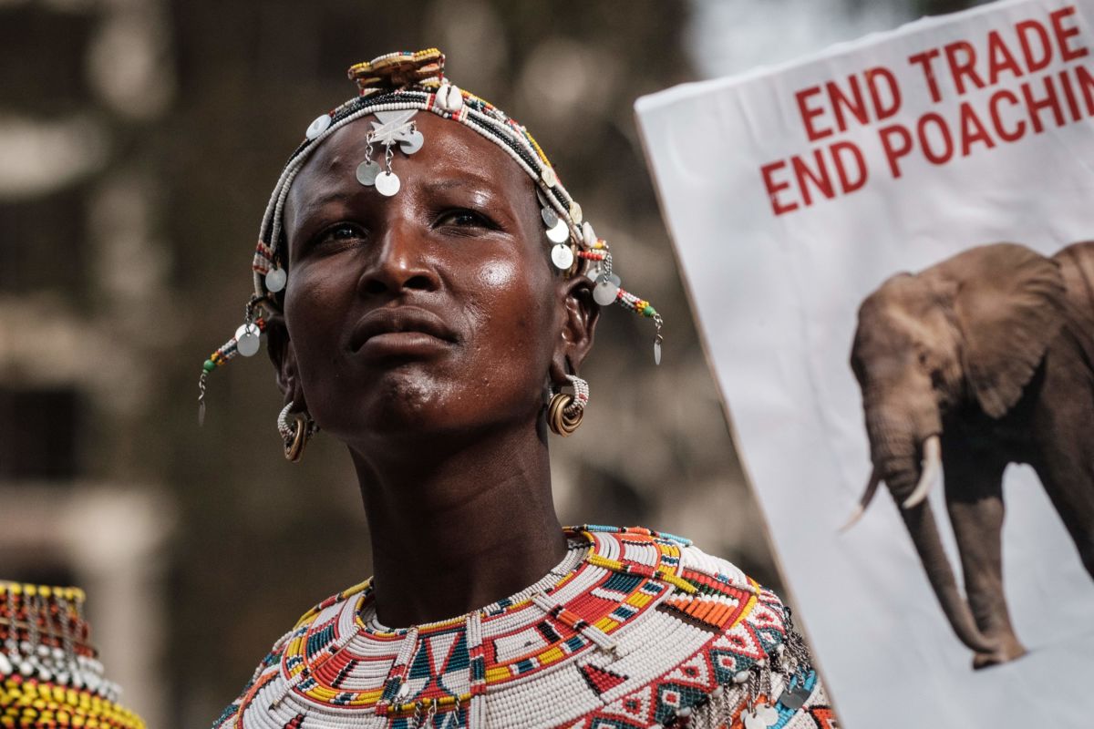 An Indigenous Kenyan woman stands near a sign denouncing elephant poaching during a protest