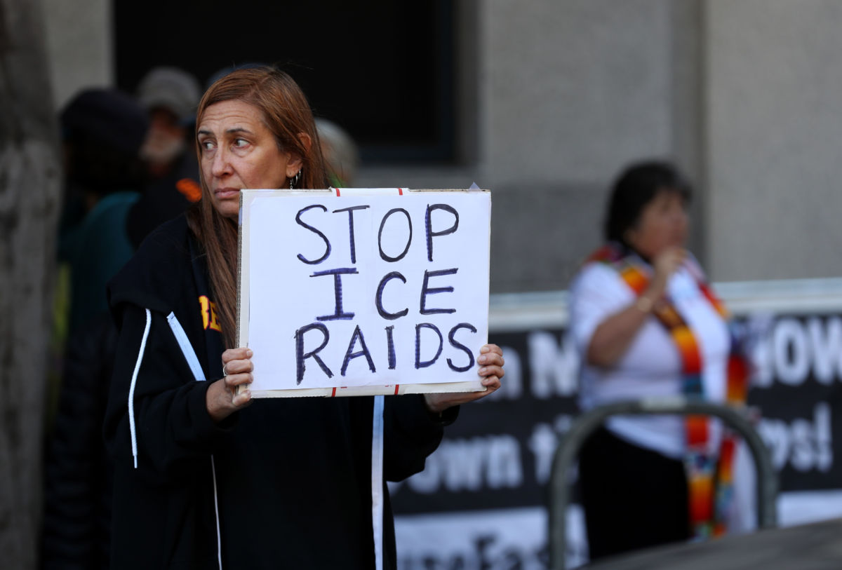 A woman holds a sign reading "STOP ICE RAIDS"