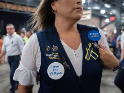 A woman wears a walmart vest with various pieces of flair commemorating the victims of the mass shooting in el Paso, Texas.