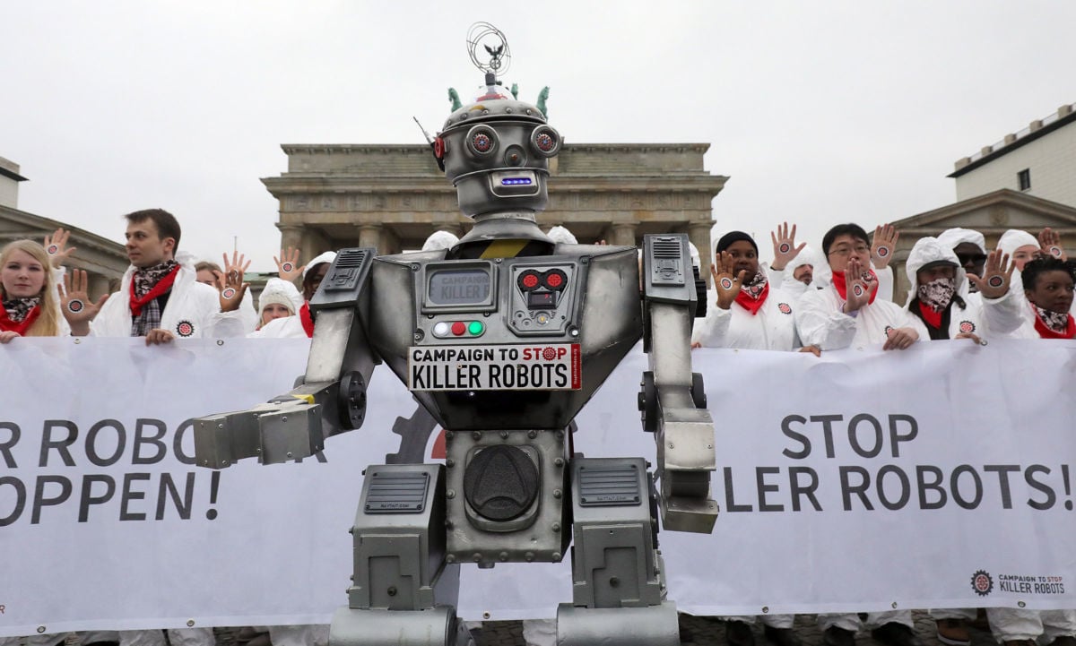 Activists clad in white clothing stand behind a robot puppet with a sign reading "STOP KILLER ROBOTS"