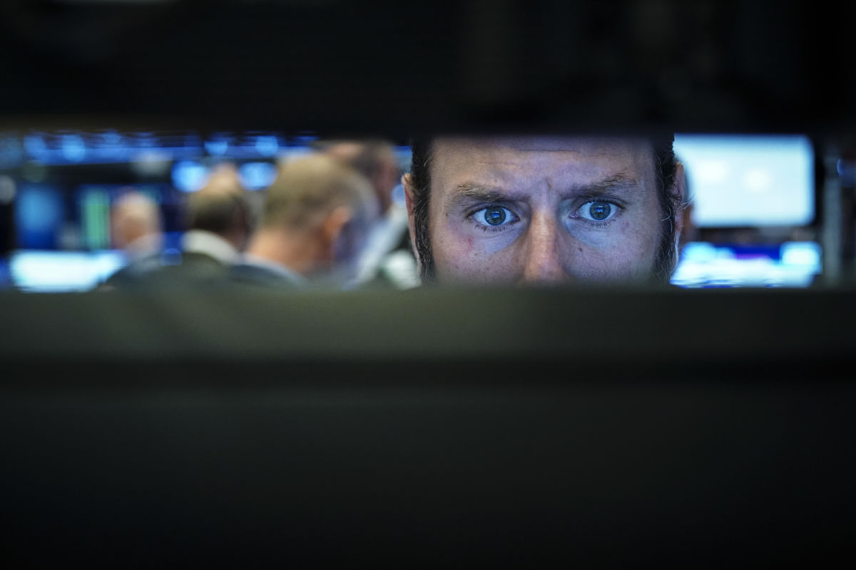 Stock broker's eyes are seen through the gap of the computer screens he's working at