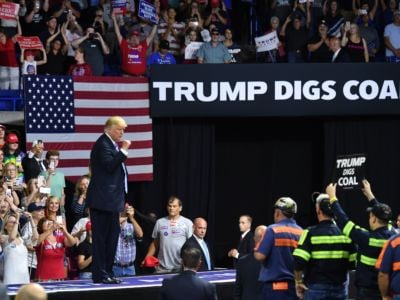 Donald Trump stands in front of a sign reading "TRUMP DIGS COAL" during a rally