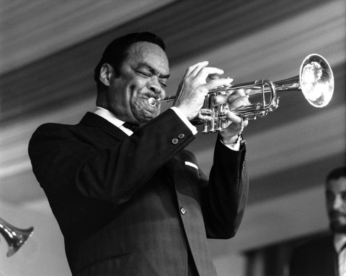 Buck Clayton plays the trumpet in a black and white photo
