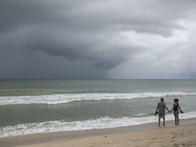 Two people hold hands as they look out onto a storm over the ocean