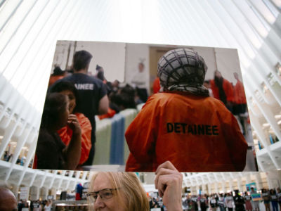 A protester holds an enlarged photo of migrants in orange jumpsuits