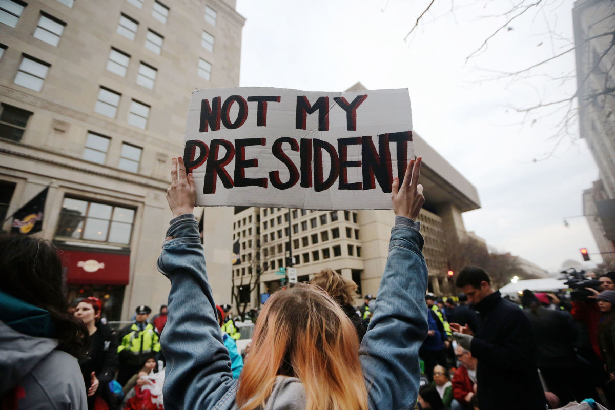 A woman holds a sign reading "NOT MY PRESIDENT" during a protest