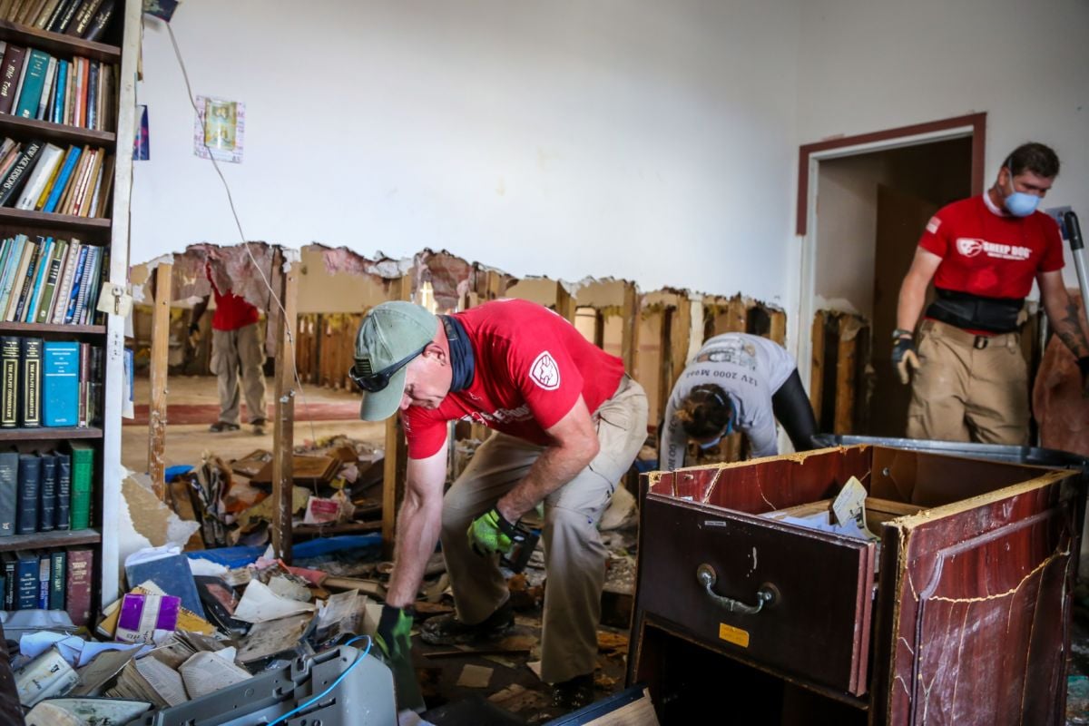 Workers in red shirts clear debris from a damaged church damaged during hurricane dorian