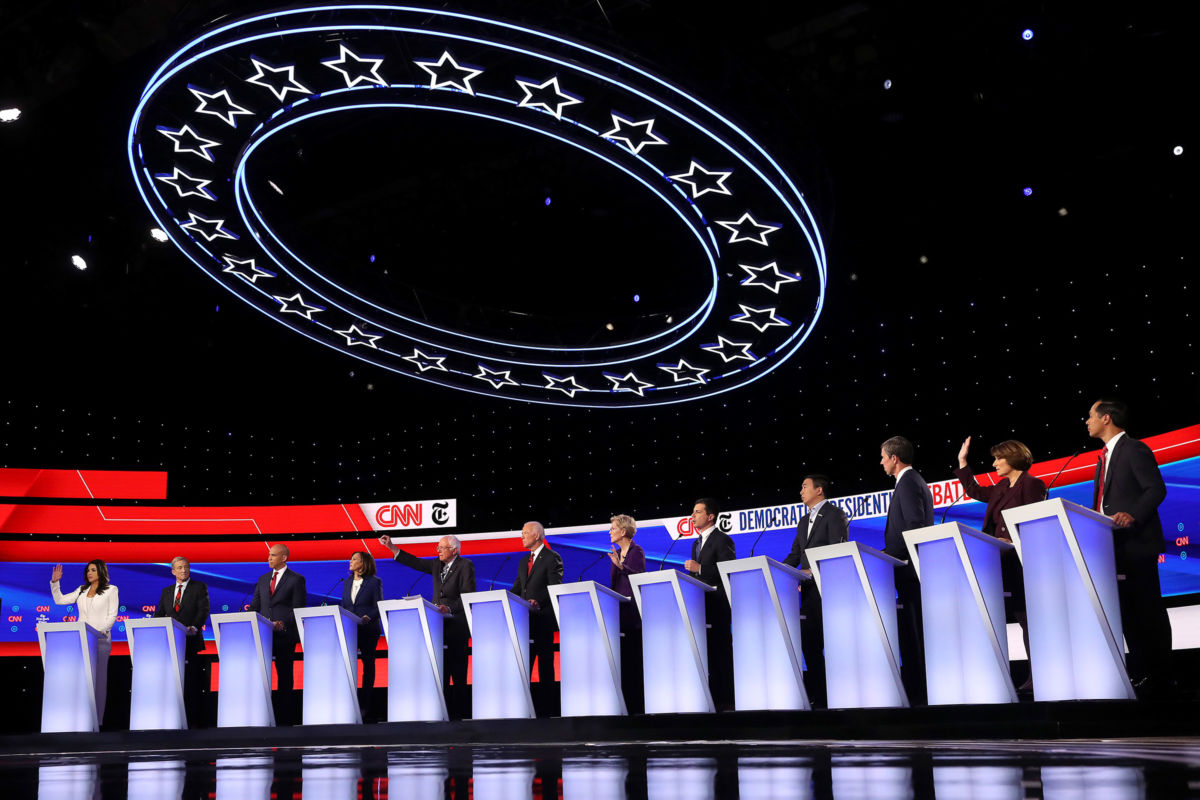 Democratic presidential candidates stand in a line behind their respective podiums