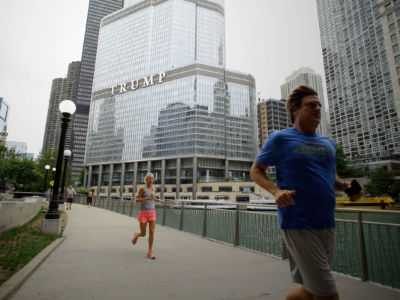 Runners exercise on the riverwalk in front of Trump Tower in the background