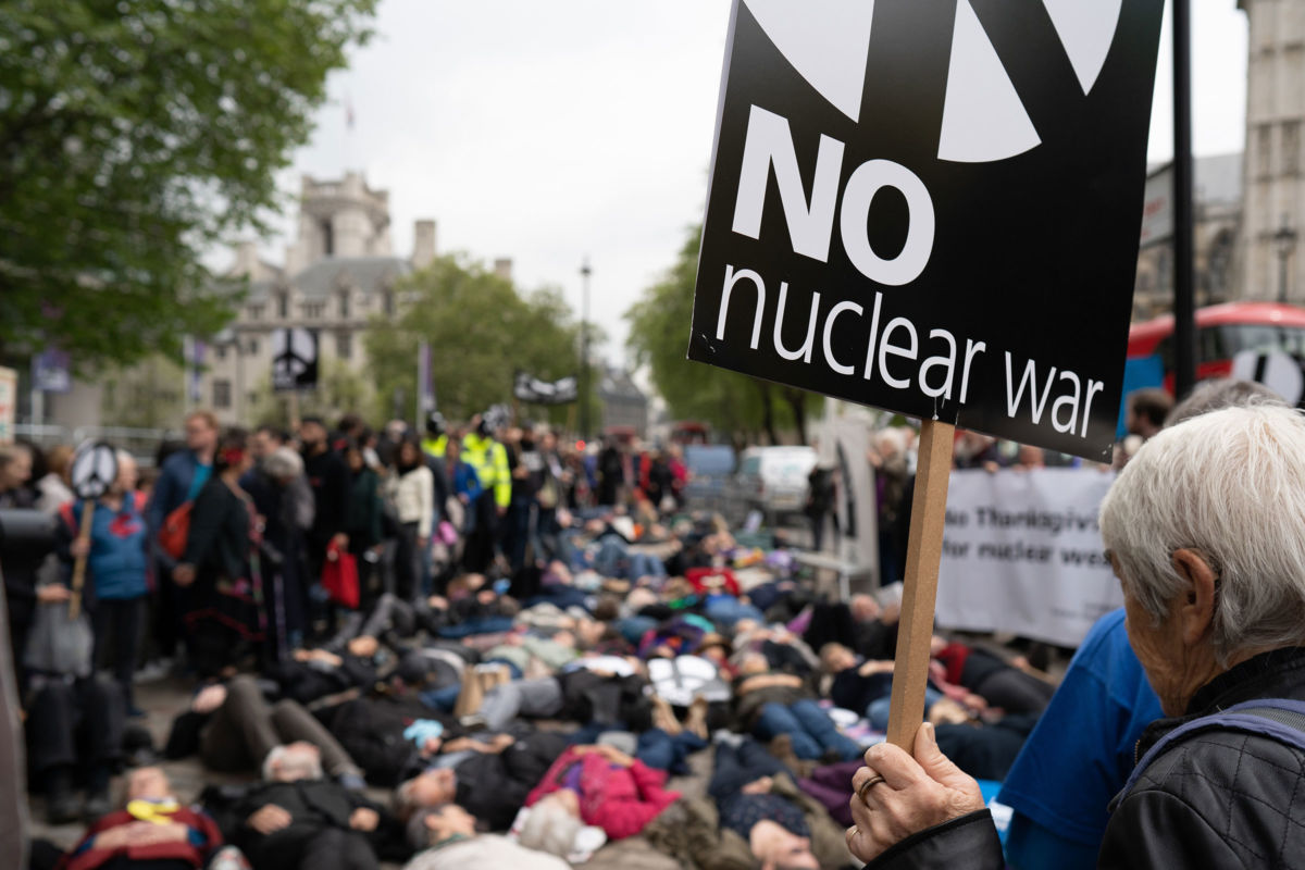 An activist holds a sign reading "No nuclear war" while others lie in the street in protest