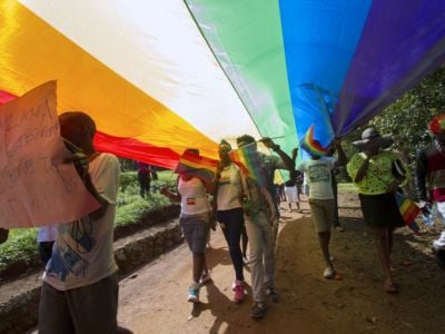 People walk beneath a large stretched out rainbow flag