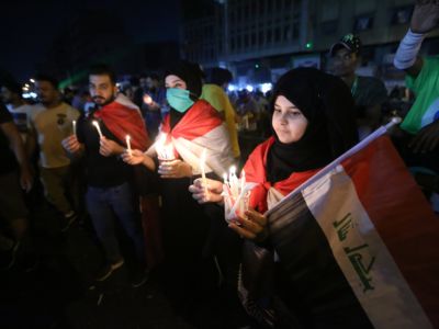 A girl in a hijab holds the Iraqi flag and a small cup of candles alongside other protesters doing the same