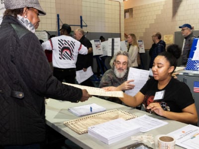 A young woman accepts the cast ballot of an older voter