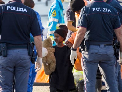 A young girl clutching a teddy bear stands between to police officers