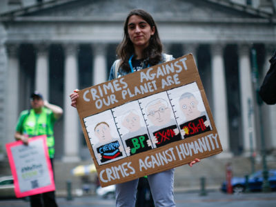 An activist carries a sign reading "CRIMES AGAINST OUR PLANET ARE CRIMES AGAINST HUMANITY" during a protest