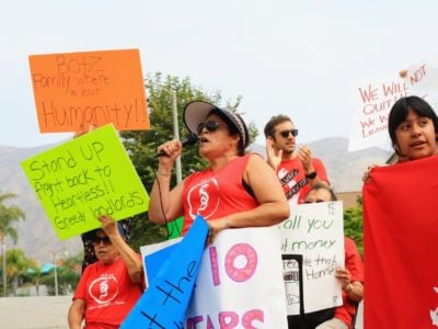 A woman in red speaks into a micophone while surrounded by others displaying colorful signs