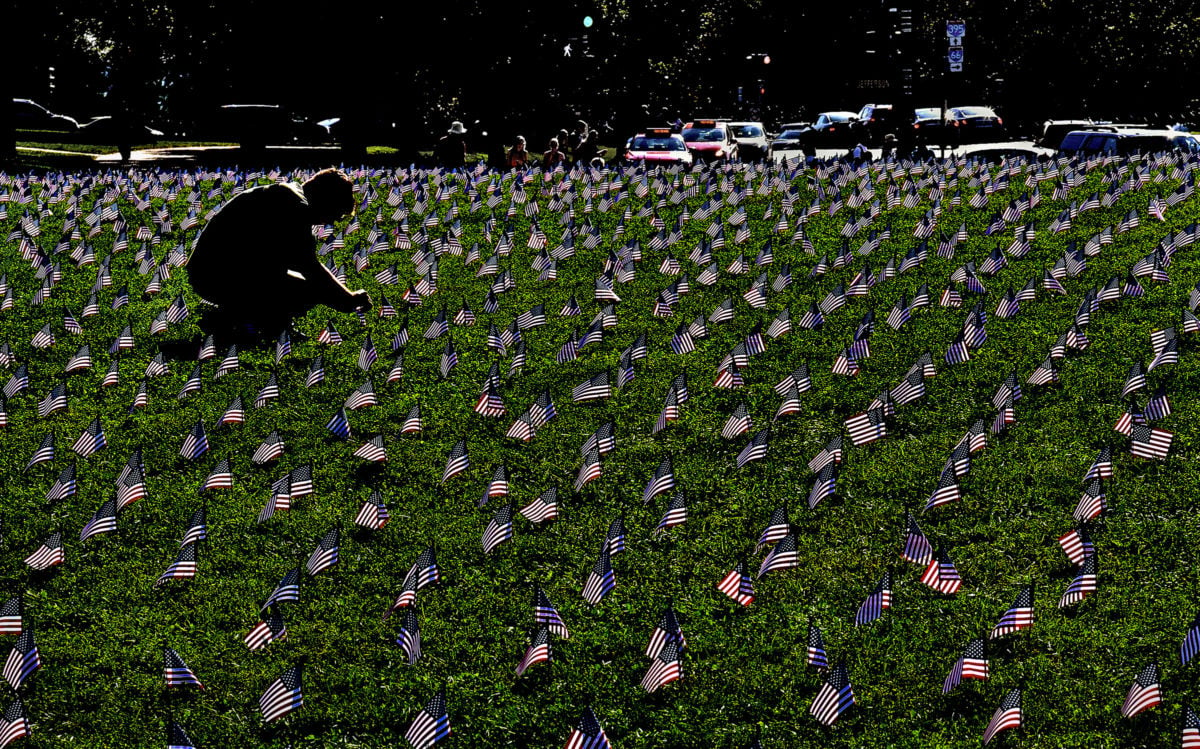 A silhouetted figure kneels in the grass to plant a small u.s. flag in the ground