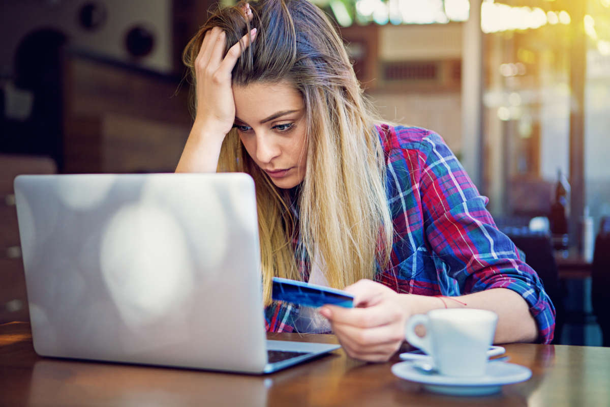 A woman looks stressed at her computer while holding a credit card