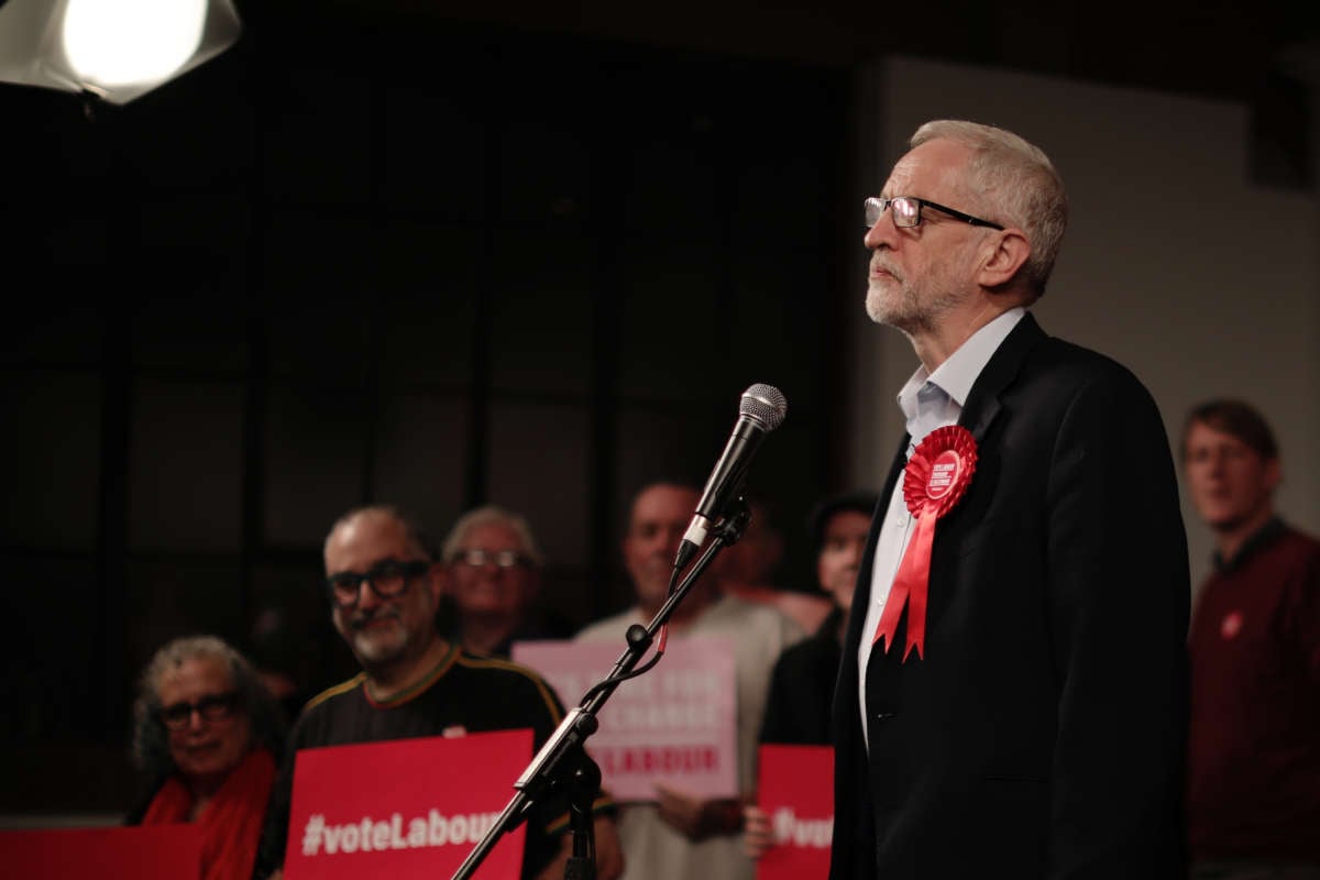 Jeremy Corbyn stands behind a microphone while surrounded by supporters