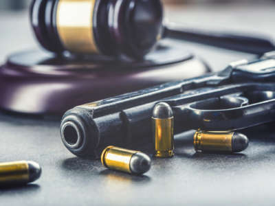A gun and bullets lie on a table in front of a gavel