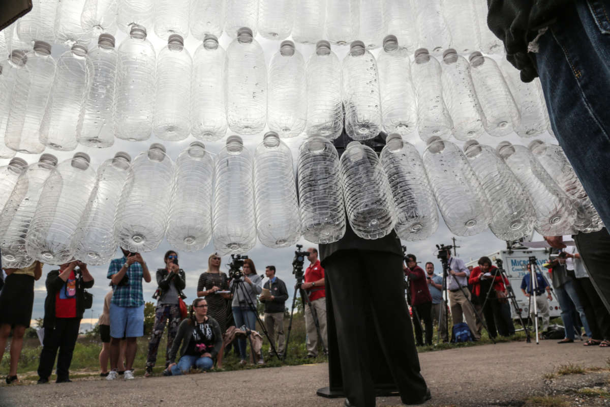 A speaker stands in front of a wall of empty plastic water bottes