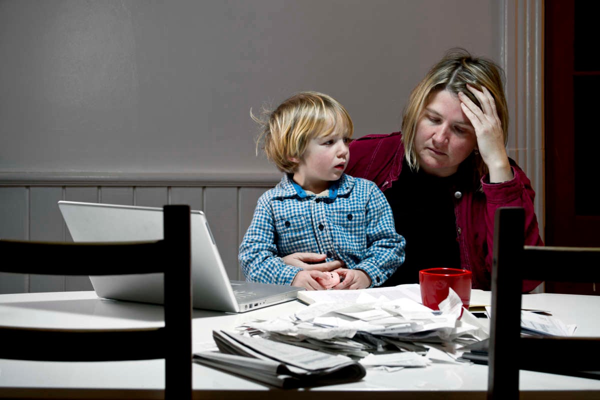 A woman sits with her child on her lap while looking despondently at bills