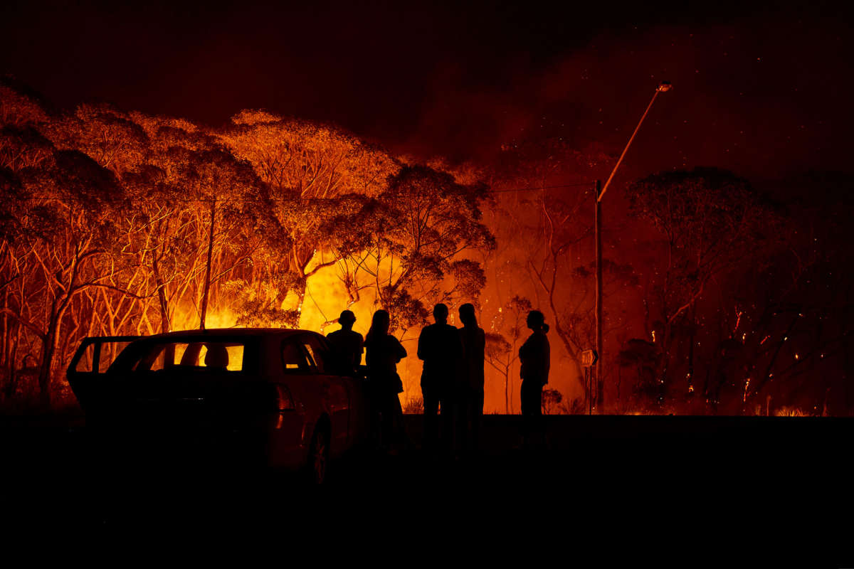 Residents look on as flames burn through bush on January 4, 2020, in Lake Tabourie, Australia.