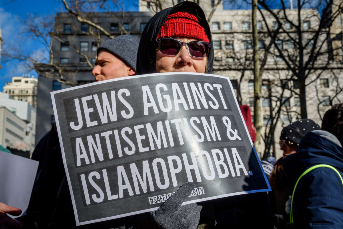 A woman holds a sign reading "JEWS AGAINST ANTISEMITISM AND ISLAMOPHOBIA" during a rally