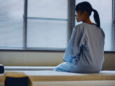 A woman in a hospital gown sits on a bed